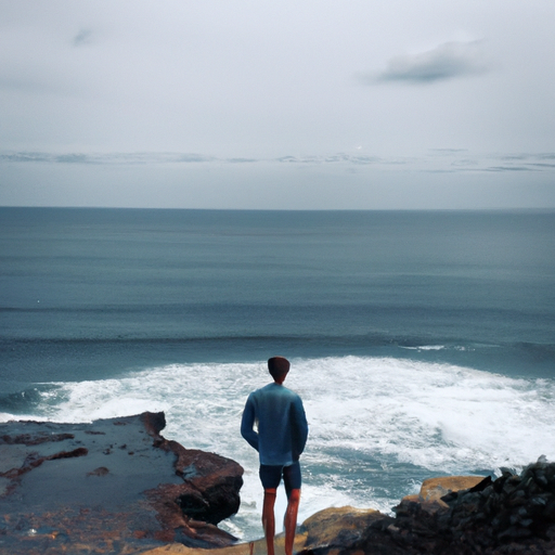 A photo of a person standing at the edge of a cliff looking out at the ocean